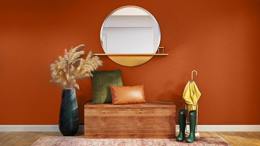photo of a large rusty orange terracotta wall, with a wooden bench placed on top of it, decorated with green and orange cushions, pampas grass on the left and rain boots and umbrella to the right, with a round mirror above it