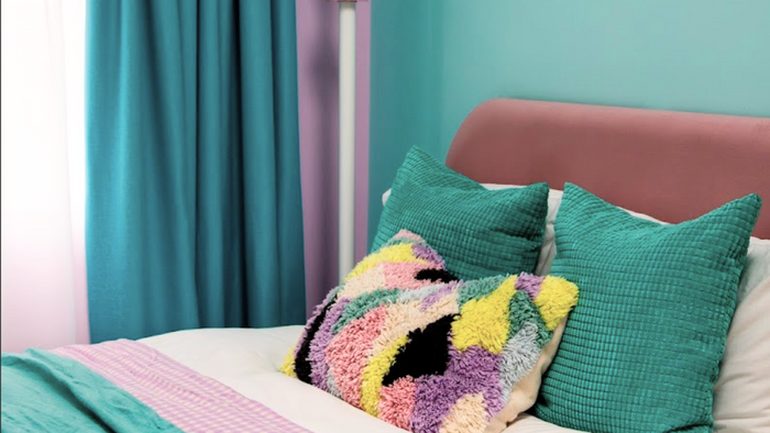 Colorful bedroom with pink walls, teal curtains, and multicolored pillows on a bed.
