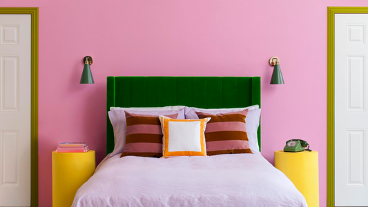 Pink bedroom with green velvet bed and symmetrical lighting and doors.