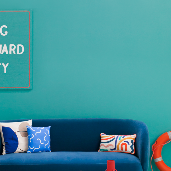 photo of a navy blue teal sofa photographed in the middle of a teal wall, with an orange ladder and life ring on the right and a sign saying 'warning no lifeguard on duty' on the left