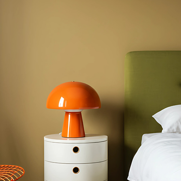 bedroom interior image with a muted yellow wall and photographed olive green bed, bright orange chair, white round bedside table and a bright orange night lamp