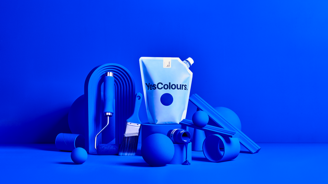 multiple home decor and DIY objects - paint roller, paint brush, as well as small objects in various shapes, all painted in ultramarine blue colour and arranged around a white pouch with logo YesColours