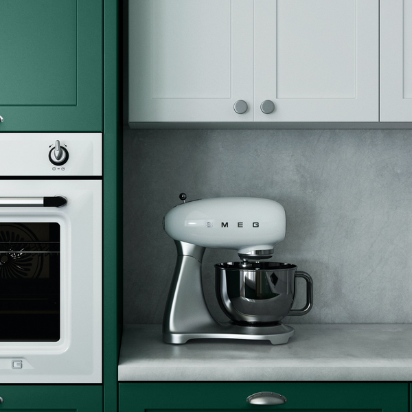 a minimalist kitchen with dark green painted cupboards, integrated oven on the left side, white kitchen cupboards in the middle and a concrete blacktop and countertop with a white Smeg mixer and small vase placed on top