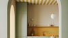 A modern kitchen interior with a sage green cabinet, mustard yellow backsplash, striped yellow and white ceiling, and a white pendant light.